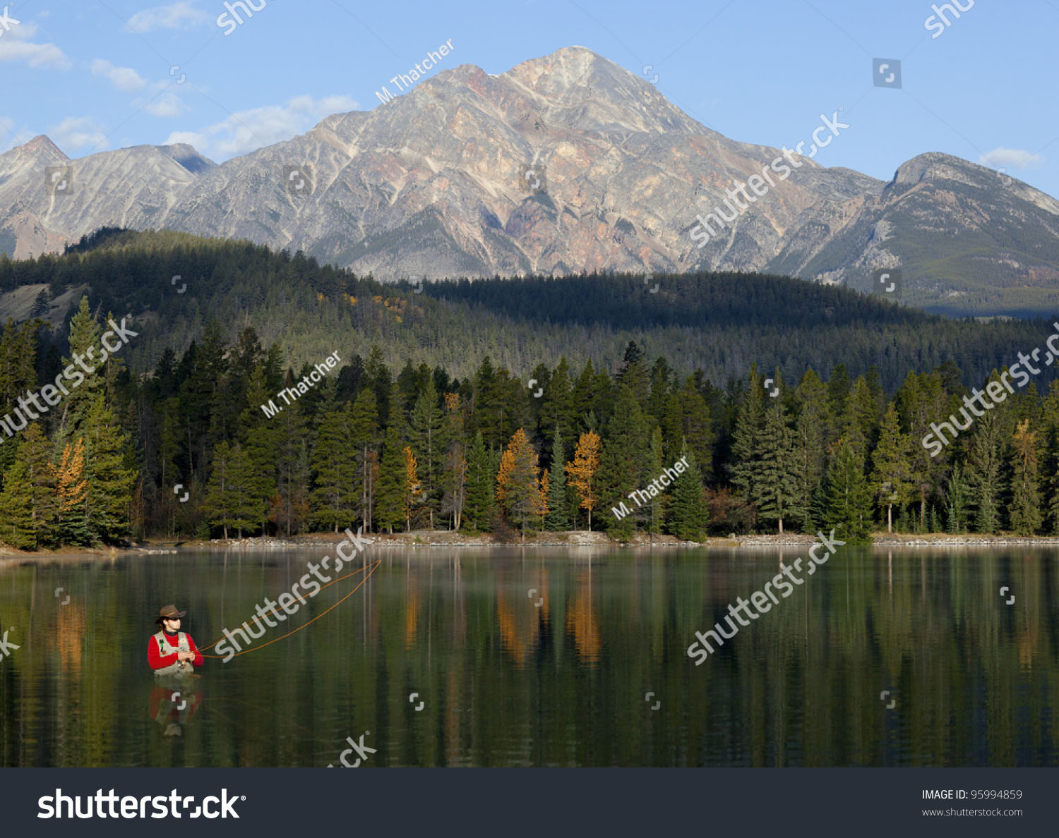 stock photo man waist deep in water fishing with reflections and mountains in background 95994859